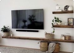 a flat screen tv sitting on top of a wooden shelf next to potted plants