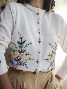 a close up of a person wearing a white sweater with colorful flowers on the front