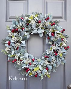 a wreath with red berries and greenery is hanging on the front door for christmas