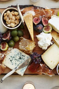 a wooden board topped with lots of different types of cheese and meats next to olives