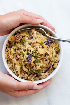 two hands holding a white bowl filled with food