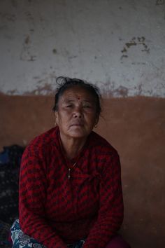 an old woman sitting on the ground in front of a wall