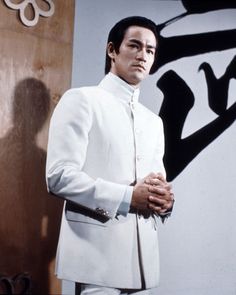 a man in a white suit standing next to a wall with chinese writing on it