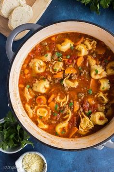 a pot filled with pasta and meat soup on top of a blue table next to bread