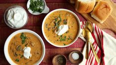 two bowls of soup on a table with bread, sour cream and spoons next to it