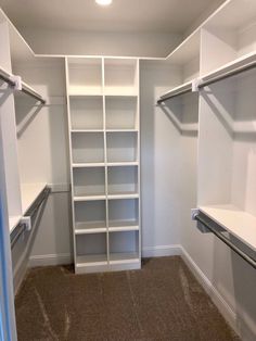 an empty walk in closet with white shelving and carpeted flooring is shown