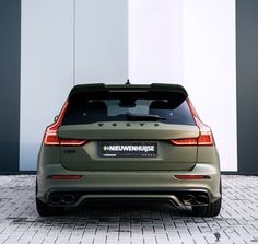 the back end of a green car parked in front of a white and gray building