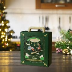 a green box sitting on top of a wooden table next to a christmas tree and other decorations