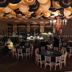 a room filled with tables and chairs covered in black, white and gold balloons hanging from the ceiling