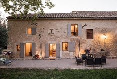 an old stone house with patio and dining table in the front yard at night time