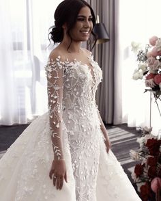 a woman in a white wedding dress standing next to a flowered wall and window