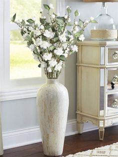 a white vase filled with flowers sitting on top of a wooden floor next to a dresser