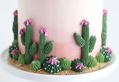 a cake decorated with pink frosting and green cactus decorations on a white platter