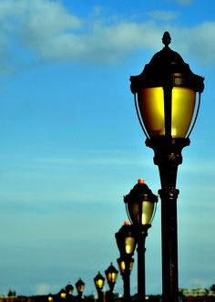 a street light sitting on the side of a road under a blue sky with clouds