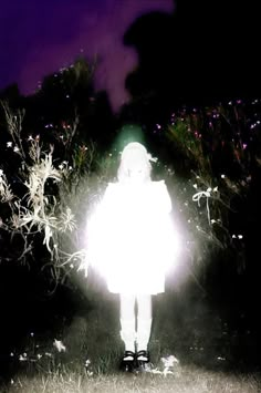 a person standing in the grass with a light shining on their face and hands behind them