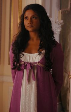 a woman with long hair wearing a purple and white dress standing next to a wall