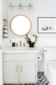 a white bathroom with black and gold accessories on the vanity, round mirror above it