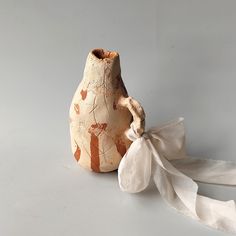 an old vase with a white ribbon tied around it on a gray surface, next to a piece of cloth