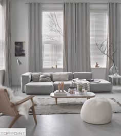 a living room filled with furniture and windows covered in white drapes, along with a rug on the floor