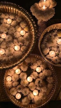 three metal trays filled with lit candles on top of a wooden table covered in frosted flowers