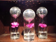 three glass vases with pink flowers in front of a disco ball on a shelf