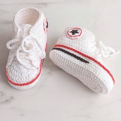 two crocheted baby shoes are sitting on a marble surface, one is white and the other is red