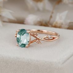 a ring with an oval cut green stone and leaves on it, sitting on a white surface