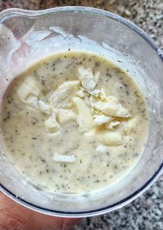 a hand holding a glass bowl filled with broccoli and cheese soup on top of a granite countertop