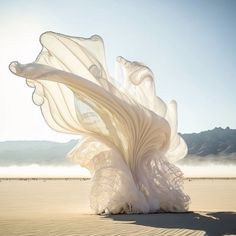 a large white piece of art sitting on top of a sandy beach next to the ocean