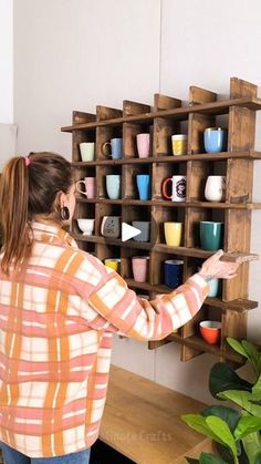 a woman standing in front of a wooden shelf filled with cups