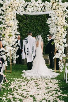 a bride and groom walking down the aisle at their wedding ceremony in front of an archway with white flowers