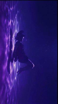 a woman standing in front of a wall with purple lights on it and her legs up