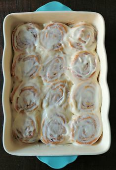 a pan filled with cinnamon rolls on top of a blue plate next to a wooden table