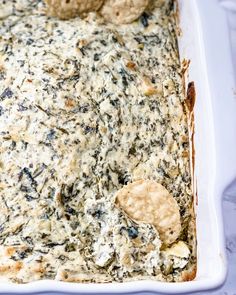 a casserole dish with spinach, cheese and crackers in it on a table