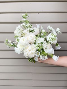 a bouquet of white flowers is being held by someone's arm against a wall