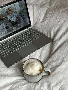 an open laptop computer sitting on top of a bed next to a cup of coffee