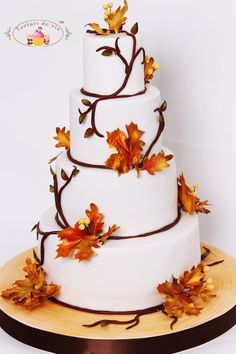 a three tiered wedding cake with fall leaves on the top and bottom, sitting on a wooden platter