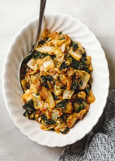 a white bowl filled with food on top of a gray tablecloth next to a fork