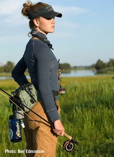 a woman is standing in the grass with her fishing gear