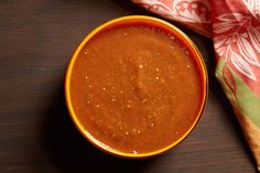 an orange bowl filled with sauce sitting on top of a wooden table next to a red and white towel