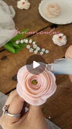 a person is cutting paper flowers with scissors on a wooden table next to white and pink flowers