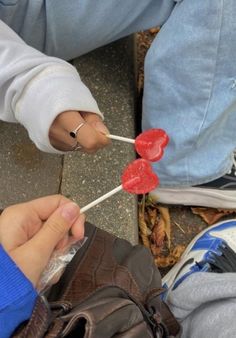 two people holding lollipops in their hands while sitting on the ground next to each other