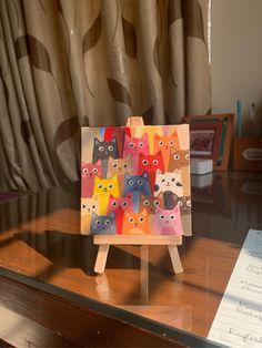 a small wooden easel with cats painted on it sitting on a table in front of a window