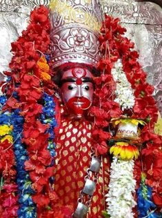 a statue with flowers around it and a person wearing a mask on his face in front of him