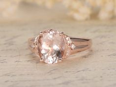 an oval morganite and diamond ring sits on a piece of paper with flowers in the background