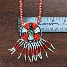 a red and white beaded necklace sitting on top of a wooden table next to a ruler