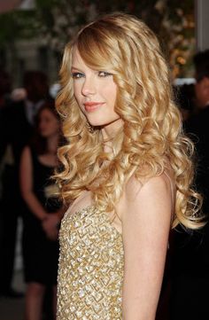 a woman with long blonde hair wearing a gold dress and posing for the camera at an event