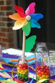 a table topped with candy and a colorful pinwheel on top of glass jars filled with candies