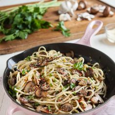 pasta with mushrooms and parsley in a skillet on a wooden table next to garlic