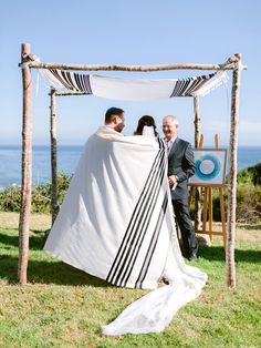 a man and woman standing under a white cloth on top of a grass covered field